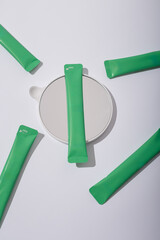 Some green cosmetics sticks on round mirror, white background. Hair repair mask mockup, unbranded template, no label. Copy space