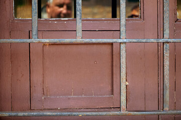 Old wooden door with metal bars, brown paint slightly worn, glass panes reveal two older men...