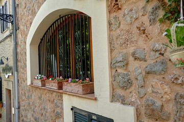 Stone wall with arched window, black wrought iron bars, and flower boxes filled with colorful...