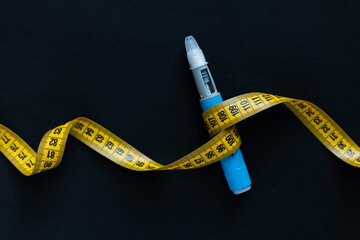 Blue insulin pen wrapped with a yellow measuring tape on black background. Symbol of diabetes,...