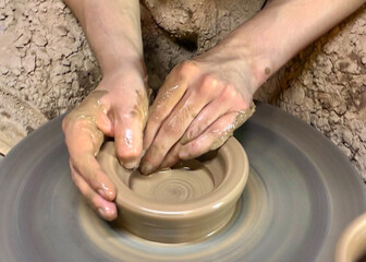Throwing pottery on wheel. Hands of young potter working with clay and making vase or pot, jug or mug. Closeup.