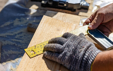 Yellow ruler placed on a wooden beam. Tools are being used to measure and mark the wooden beam for...