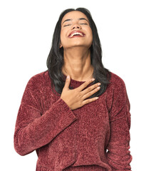 Simple portrait of a young Latina laughs out loudly keeping hand on chest.