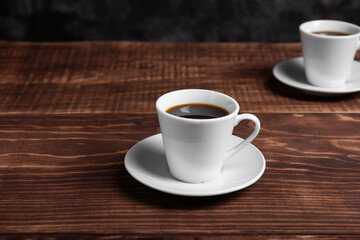 Two white cups of dark coffee sit on a rich brown wooden table.