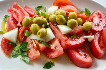 Sliced tomatoes with green olives and herbs composing a delicious salad