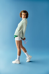 Vibrant summer fashion portrait of a young woman with curly hair on a blue backdrop