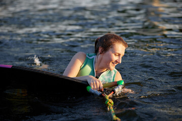 Young beautiful sporty girl in a green life jacket swims in the water with wakeboard and halyard in...