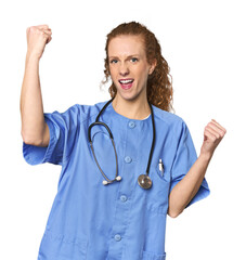 Redhead young caucasian  nurse in studio raising fist after a victory, winner concept.