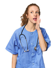 Redhead young caucasian  nurse in studio shouting and holding palm near opened mouth.