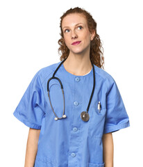 Redhead young caucasian  nurse in studio dreaming of achieving goals and purposes