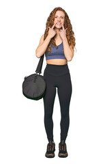 Full-body gym redhead smiles, pointing fingers at mouth.