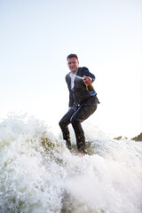 Young man in classic suit with champagne bottle rides a wakeboard on the lake near city. Happy...