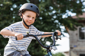 A beautiful 6-year-old boy riding a bicycle in a protective helmet outside. A happy child engaged...