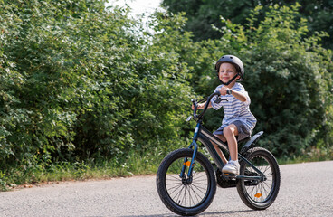 A beautiful 6-year-old boy riding a bicycle in a protective helmet outside. A happy child engaged...