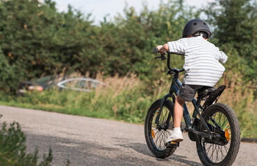 Fototapeta premium A beautiful 6-year-old boy riding a bicycle in a protective helmet outside. A happy child engaged in an active sport. Protection. Life insurance and child safety.