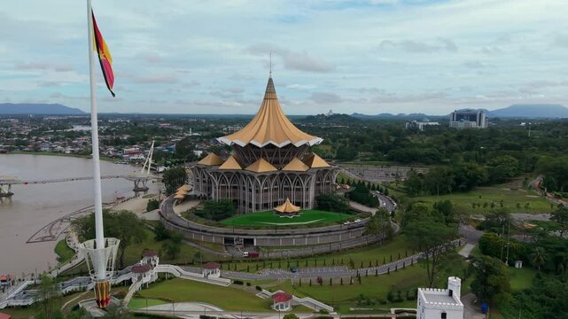 Aerial view of the sarawak state legislative assembly building with golden dome roof and modern pedestrian darul hana bridge crossing the sarawak river