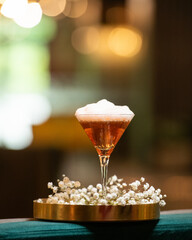 A deep amber or brown alcoholic cocktail, topped with a thick layer of white foam, is presented in...
