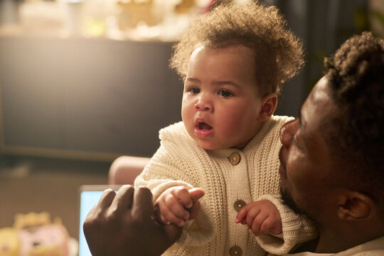 Black man holding infant child, gently supporting baby while interacting in home setting, demonstrating paternity leave concept with close family bonding moment