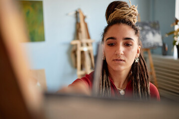 Young adult woman painting on canvas, focusing on creative process in art studio, long dreadlocks...
