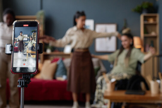 Caucasian young adult woman with disability sitting in wheelchair being filmed on smartphone while friend standing beside her with arms outstretched in living room - Powered by Adobe