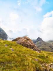 Scenic grassy hillside with rock formations leading towards Carrauntoohil peak in Ireland. Clouds...