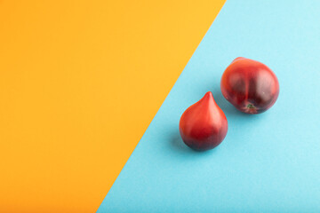 Red Heart shape tomatoes on blue and orange pastel paper. Side view, copy space