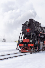 Vintage steam locomotive with a red star, surrounded by snow-covered landscape, emits steam while...