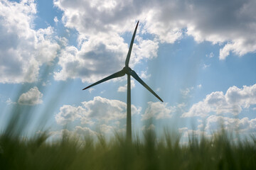 Single wind turbine silhouetted against bright blue sky with scattered fluffy clouds and blurred...
