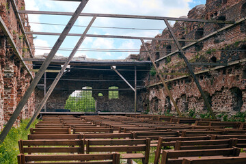 Audience wooden benches in front of stage for concerts in old ruins of Brandenburg castle of Teutonic Order in Ushakovo village, Kaliningrad region. Brick Brandenburg castle ruined after World War II