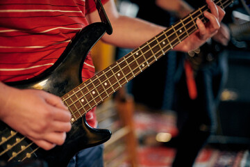 Focused view of musician hand playing bass guitar during performance, highlighting strings and frets in dim setting, musical rehearsal for new band member