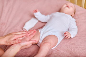 Young mother with brown hair, of caucasian descent, gently applies cream to baby girl lying on pink blanket. Bright setting emphasizes nurturing bond