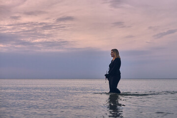 Young woman walks alone in tranquil sea under pastel sky. Her contemplative stance against soothing ocean backdrop evokes introspection and peace