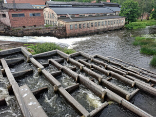 Concrete fish ladder channels water beside an old industrial building, aiding fish migration in a...
