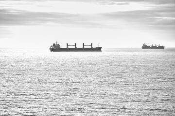Two cargo ships glide across a calm sea under a clear sky. Minimalist seascape.