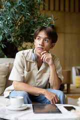 Non binary Asian student man sitting in modern coffee shop wearing headphones