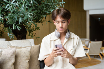Non binary Asian student man sitting in modern coffee shop using phone