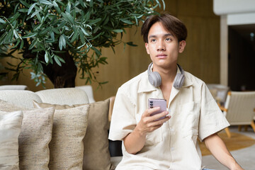 Non binary Asian student man sitting in modern coffee shop using phone