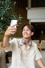 Non binary Asian student man sitting in modern coffee shop using phone