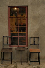Two chairs are sitting in front of a window. The chairs are old and rusted, and the table in front...