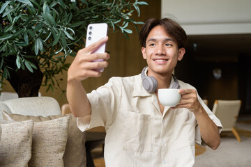 Non binary Asian student man sitting in modern coffee shop using phone