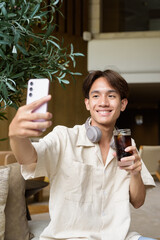 Non binary Asian student man sitting in modern coffee shop drinking cola