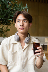 Non binary Asian student man sitting in modern coffee shop drinking cola