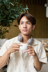 Non binary Asian student man sitting in modern cafe drinking coffee