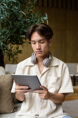 Non binary Asian student man sitting in modern coffee shop using digital tablet computer
