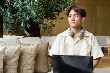 Non binary Asian student man sitting in modern coffee shop using laptop computer