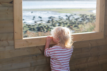 Blonde girl watching birds through a window in a birdwatching hut