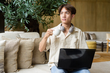 Non binary Asian student man sitting in modern coffee shop using laptop computer