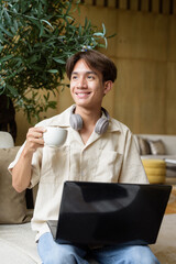 Non binary Asian student man sitting in modern coffee shop using laptop computer