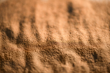 Close-up view of ground chicory root powder, revealing its rich brown color and subtle wave-like texture, creating an interesting visual pattern