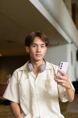 Non binary Asian student man sitting in modern coffee shop using phone